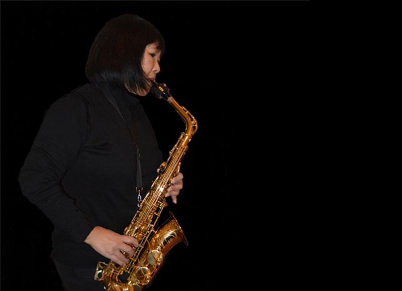 Sheila with saxophone against black background.